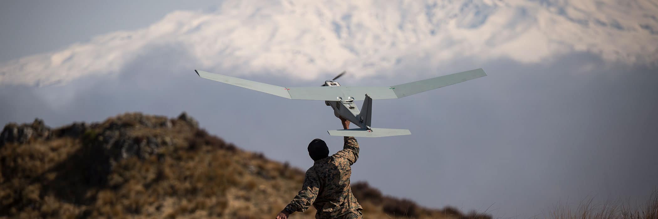 A person stands outdoors operating a drone, with mountains in the background.