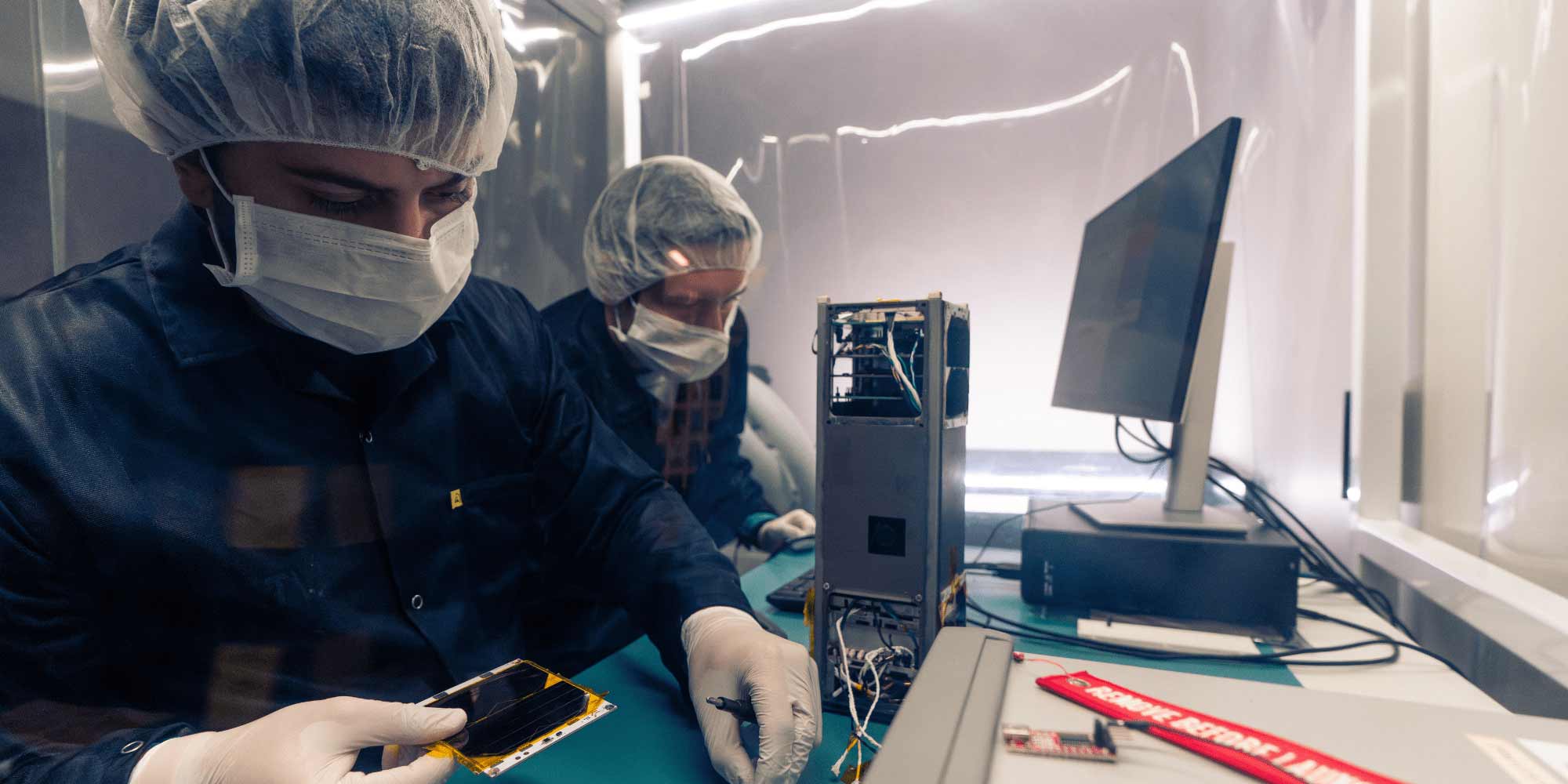 Structures Lead Frederick Wadnola (left) and Project Manager Bruce Noble (right), integrating the replacement solar panels into the CubeSat in the EagleSat Laboratory clean room. (Photo: Wilson Van Ness)