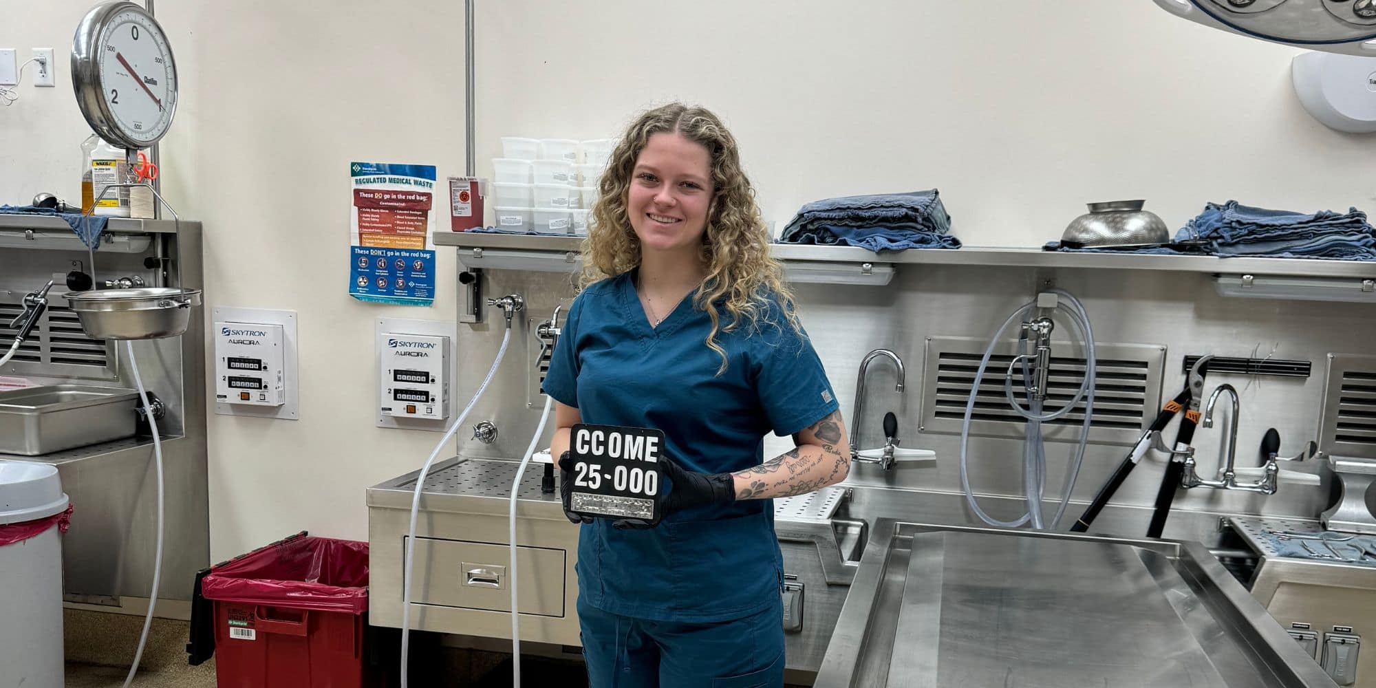 Peyton Adley stands in the autopsy suite holding a CCOME number plaque during her internship. (Photo: Peyton Adley)