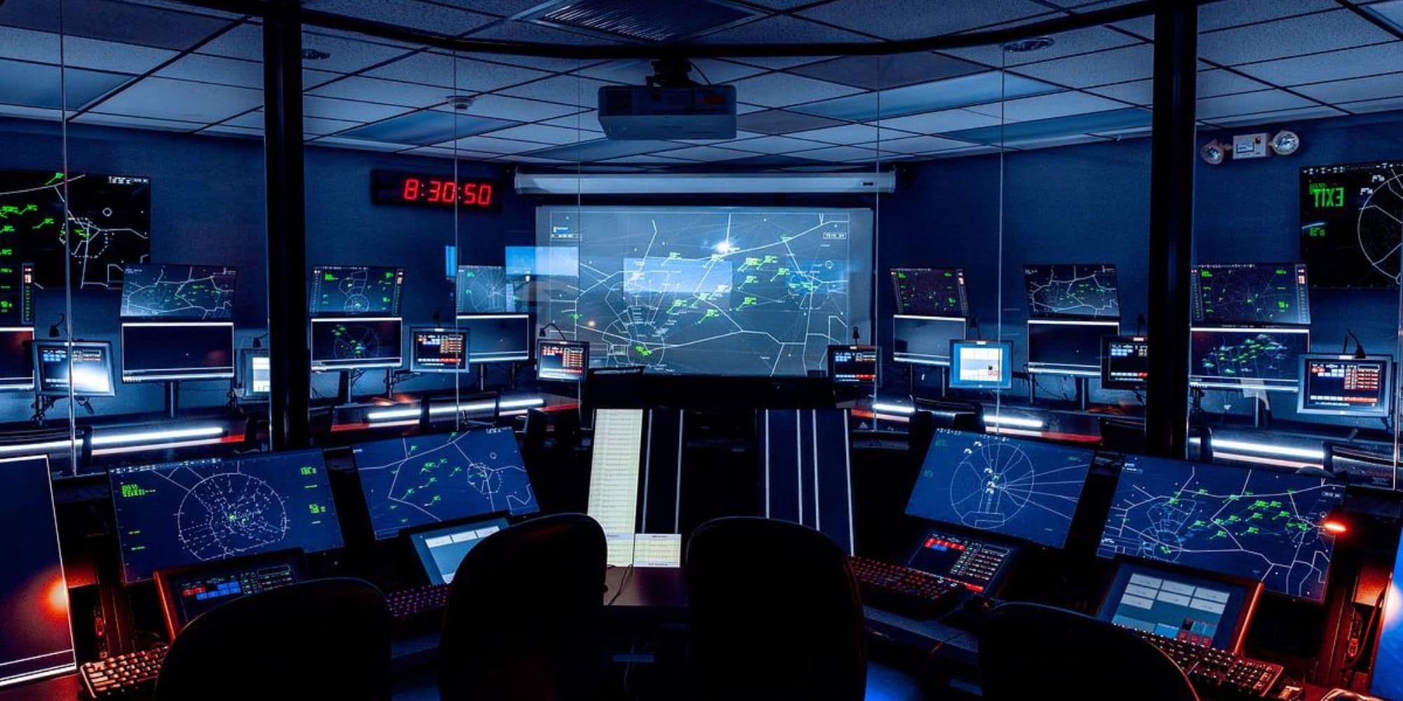 A dark room with multiple computer screens showing flight paths.