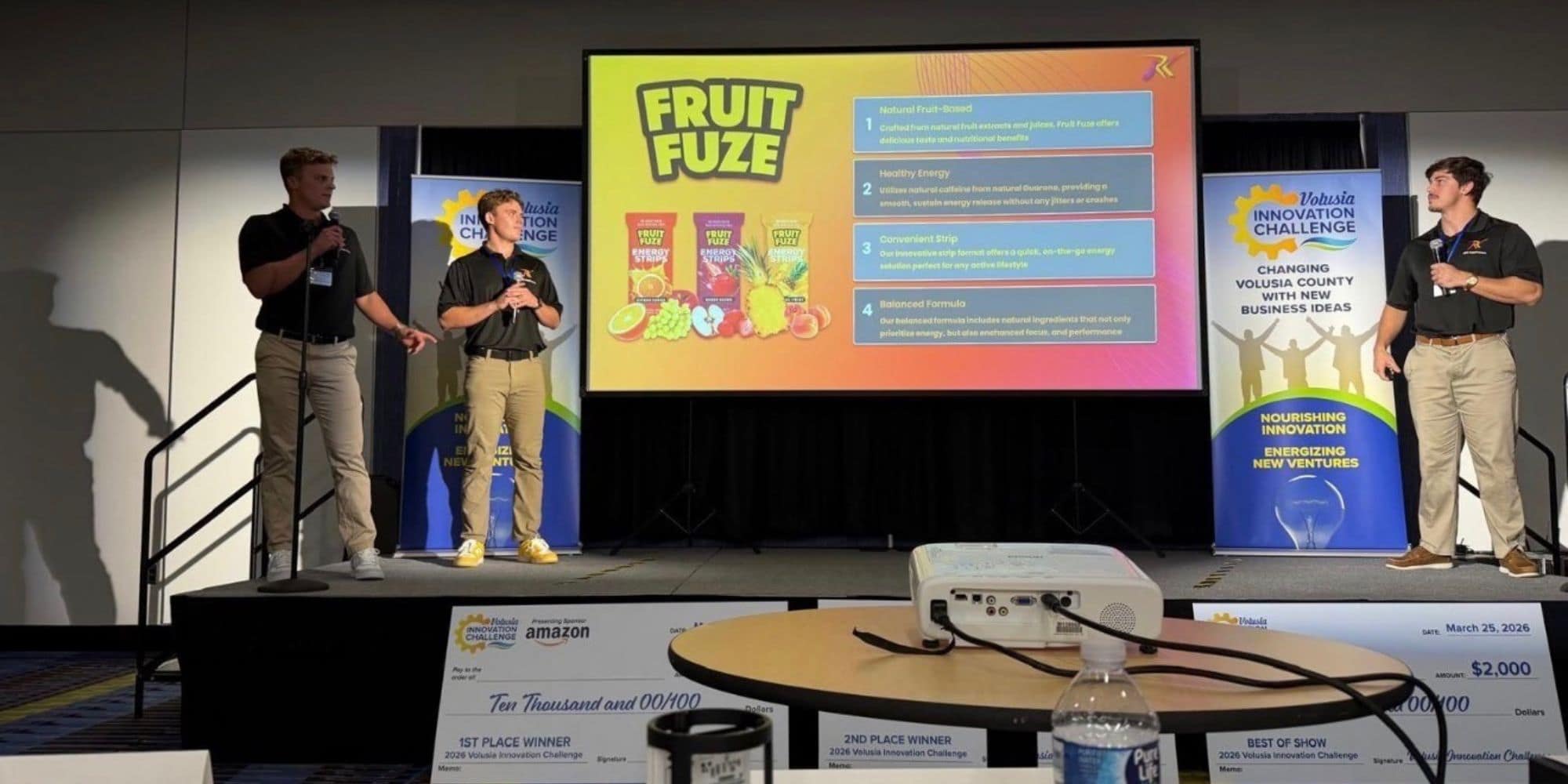 Three man stand on a small stage describing a product on a screen.