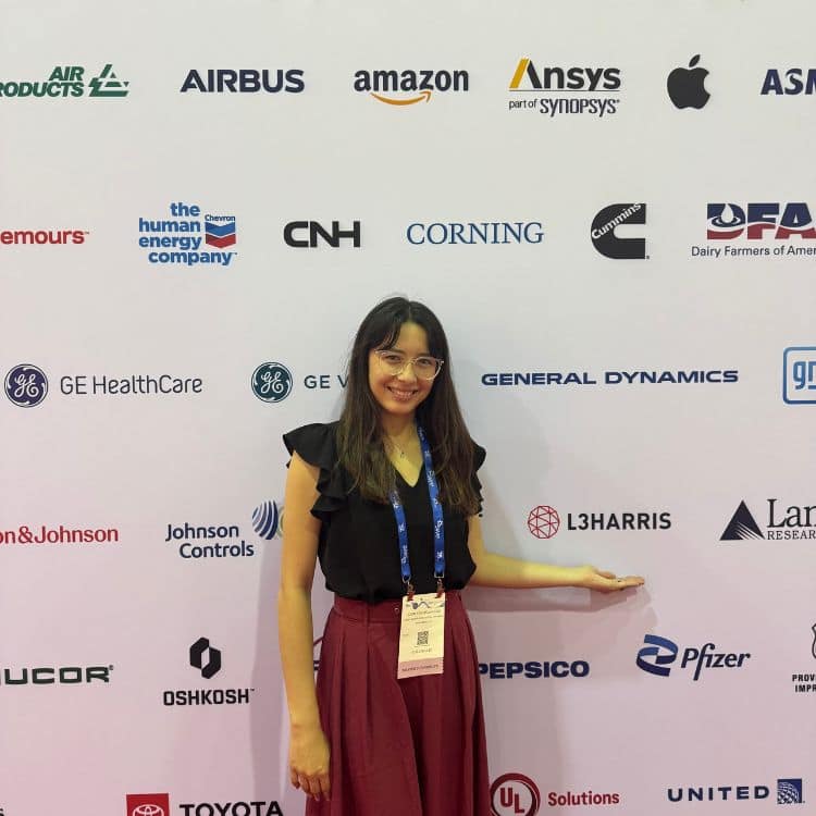 Woman stands in front of backdrop with company names on it.