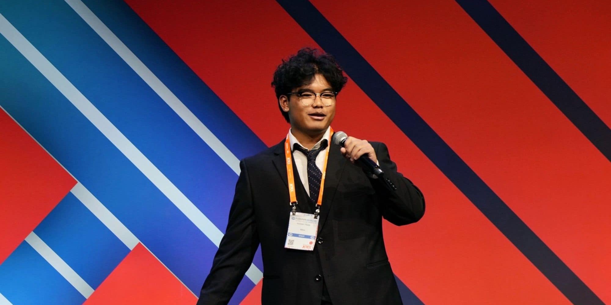 Man holds microphone on stage with red and blue background.