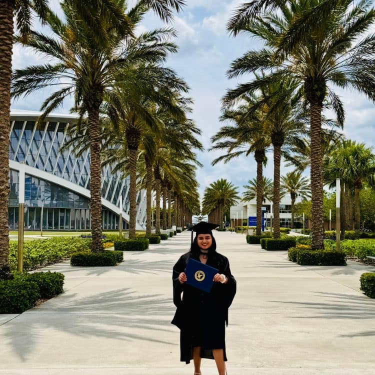 Girl stands in cap and gown on Embry-Riddle campus.