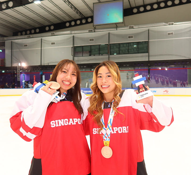 Brianna Tan holds a bronze medal on the hockey rink with a teammate