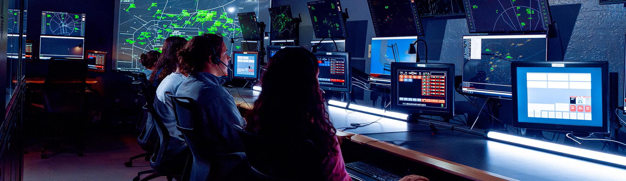 Professionals sit in a control room surrounded by large digital maps