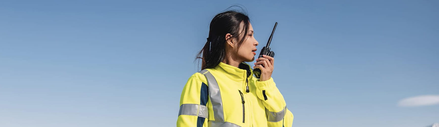 woman in a yellow safety jacket taks in a walkie talkie