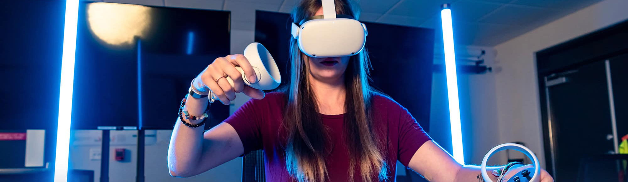 a student wears a virtual reality headset and holds controllers in her hands