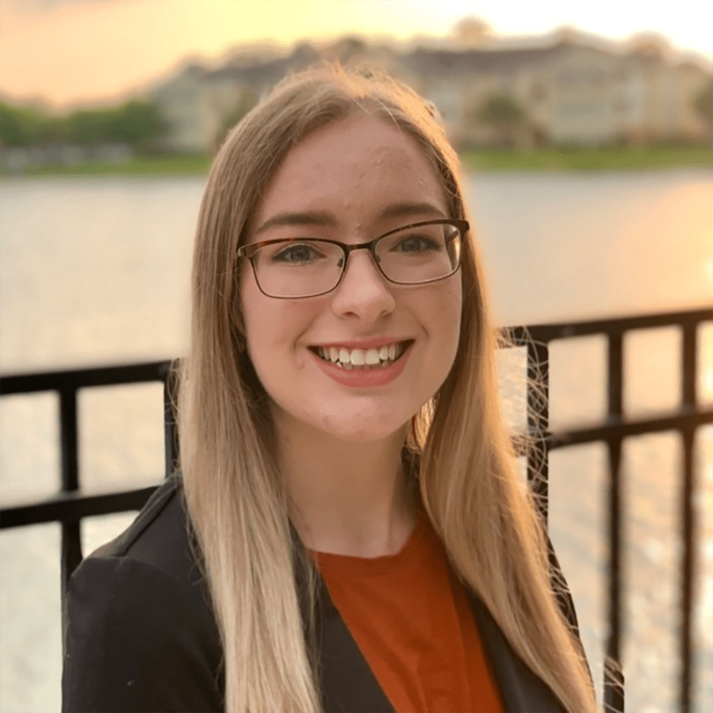Jessyca Derby stands outside in front of a river at sunset in professional dress