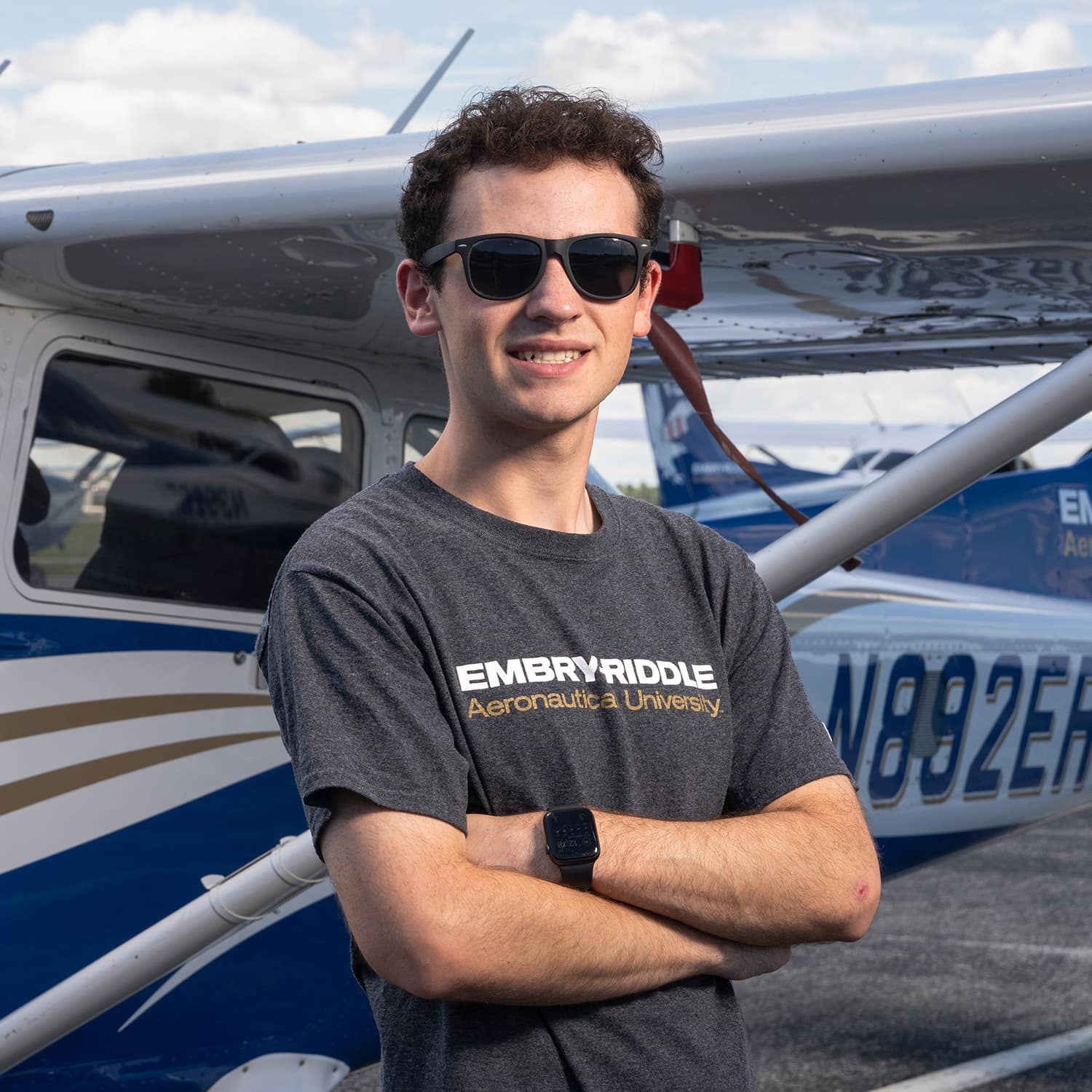 Hudson Garber stands for a photo in front of a small plane while wearing an Embry-Riddle tee shirt
