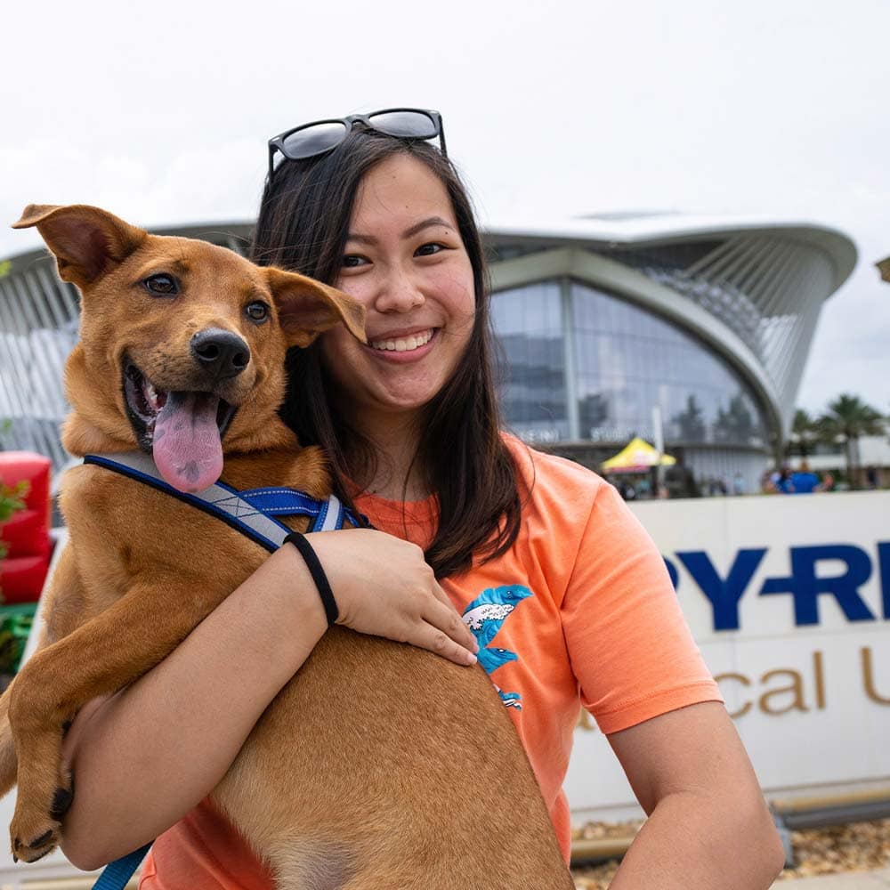 an Embry-Riddle student stands in front of a sign on campus while holding a dog