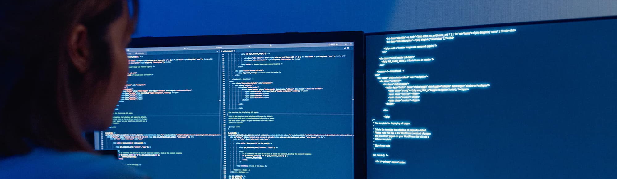 woman looks at two computer monitors with lines of code