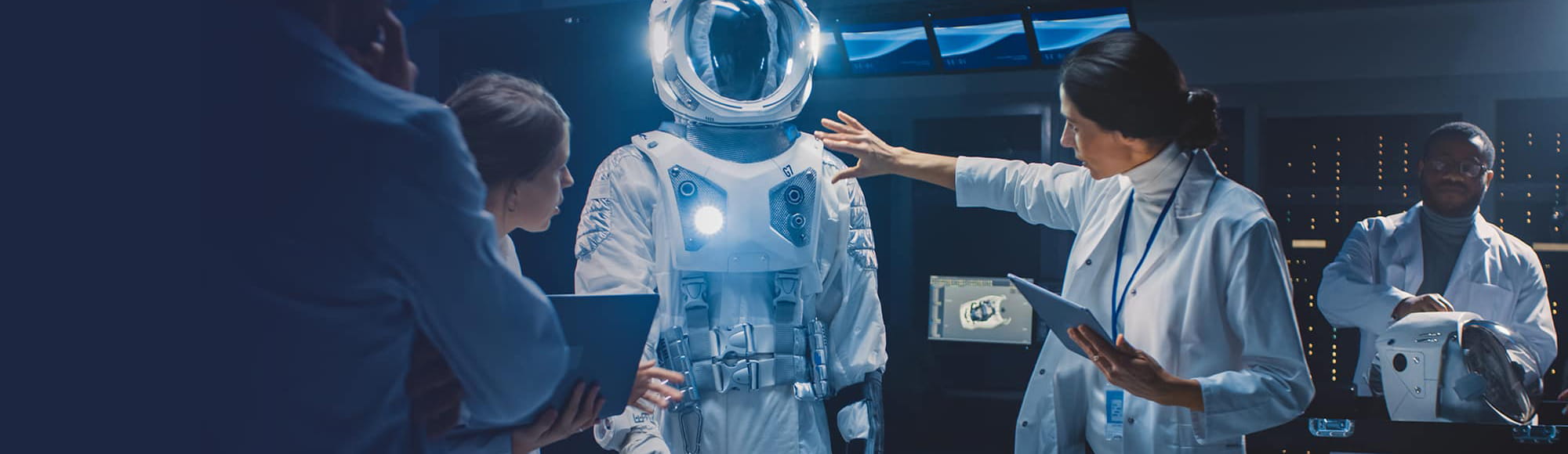 People in a lab examine a space suit while holding tablets