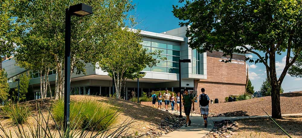 An exterior view of an Embry-Riddle Prescott campus building with students walking down the sidewalk and into the building