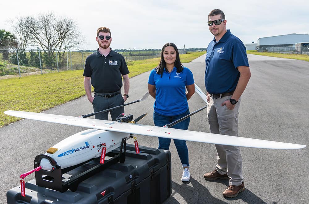 Three people stand behind a small plane. 