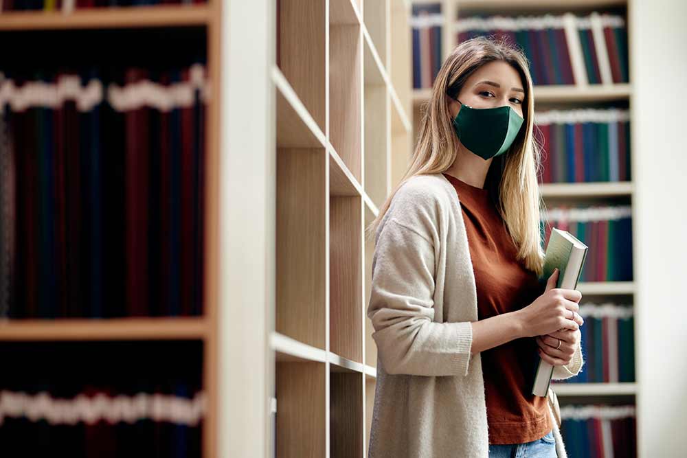 Woman wearing mask stands in library.