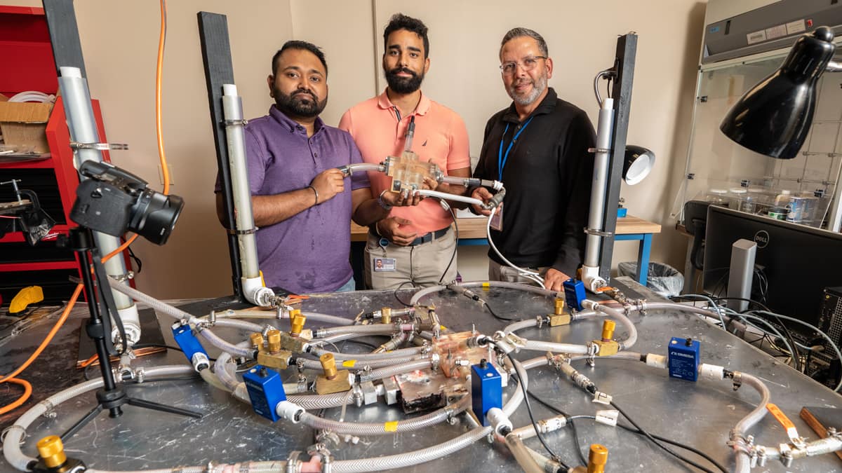 Three professors hold lab equipment in lab.