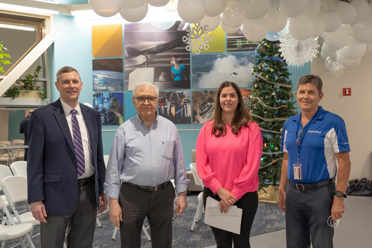 Scholarship recipient and professors pose for picture in front of Christmas tree.