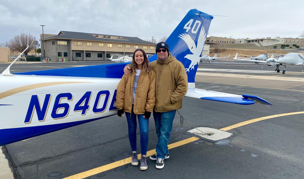 Father and daughter stand in front of plane on runway.