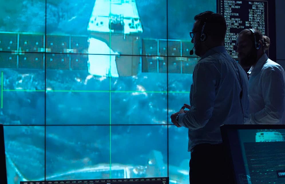 Two men look at satellite on video screen.