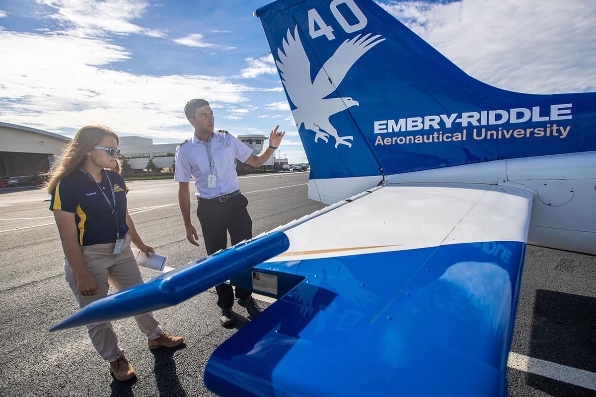 Pilot and student look at tail of airplane on runway.