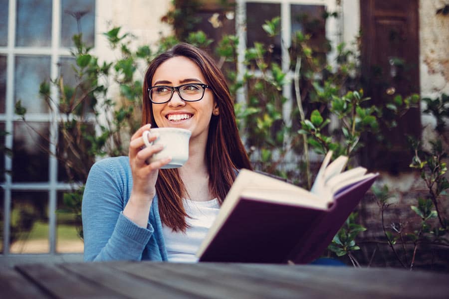 Student reading book, smiling, and drinking coffee.