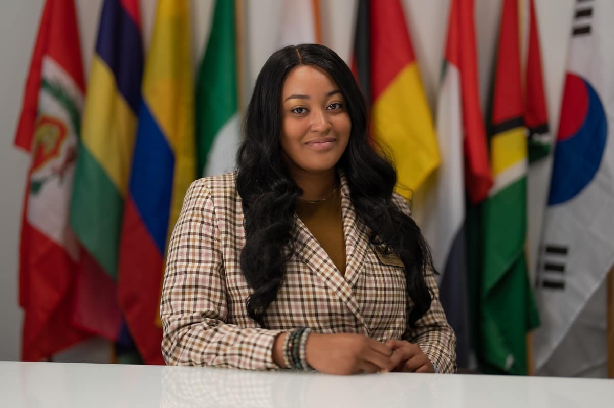 Angel Thomas poses in front of various country flags.