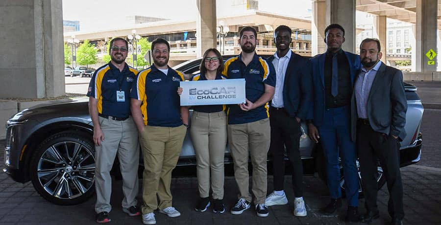 Students pose in front of a car