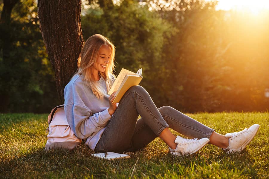 woman reads a book next to a tree in golden light.