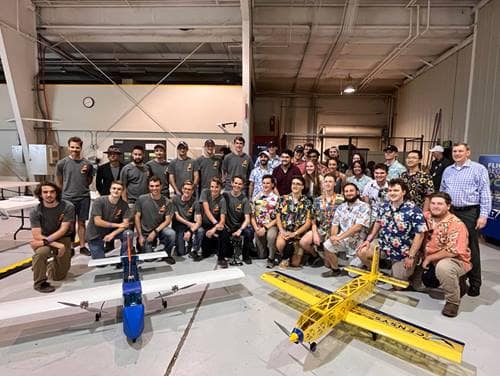 Prescott and Daytona Campus Aircraft Design teams pose behind two small aircraft.