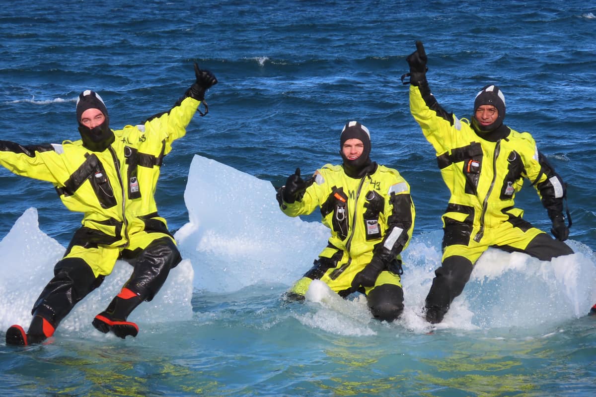 Three students sit on glacier in ocean.