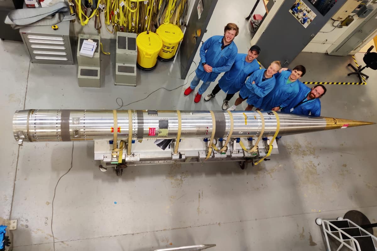 Five students stand behind small rocket.