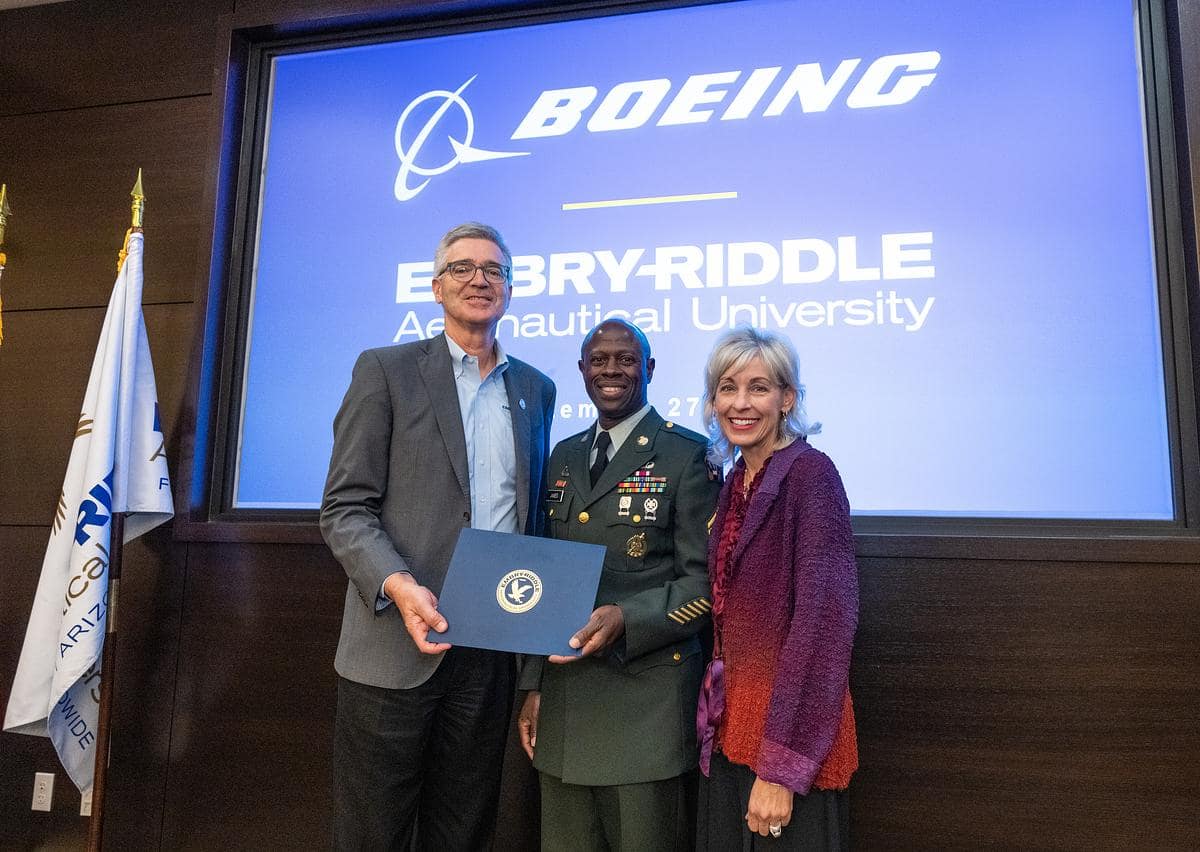 Embry‑Riddle President P. Barry Butler, Arnold James, U.S. Army retired, and Leanne Caret, executive vice president and senior advisor at The Boeing Company pose for picture on stage holding signed document.