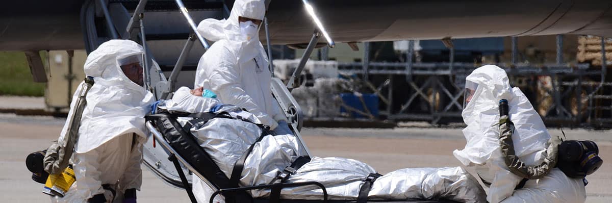 Three people in biohazard suits push a person on a stretcher.