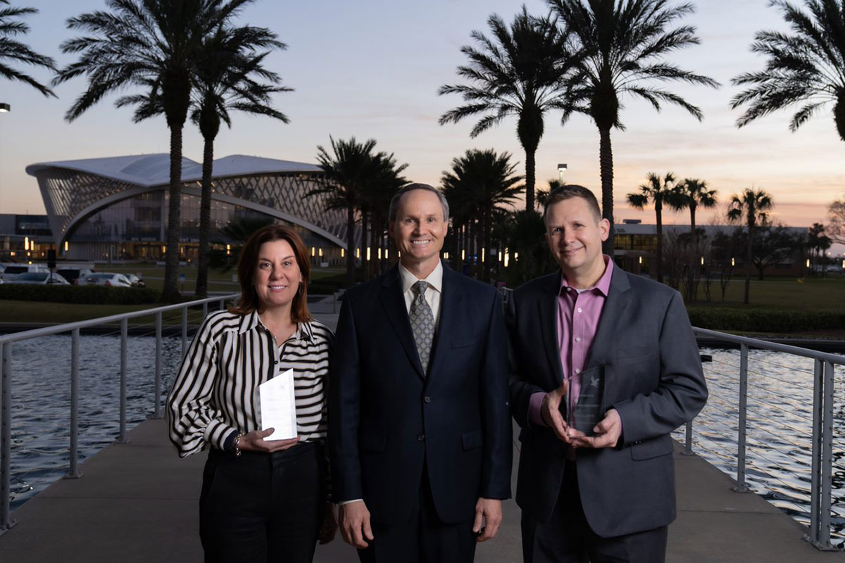 People pose with awards in front of palm trees