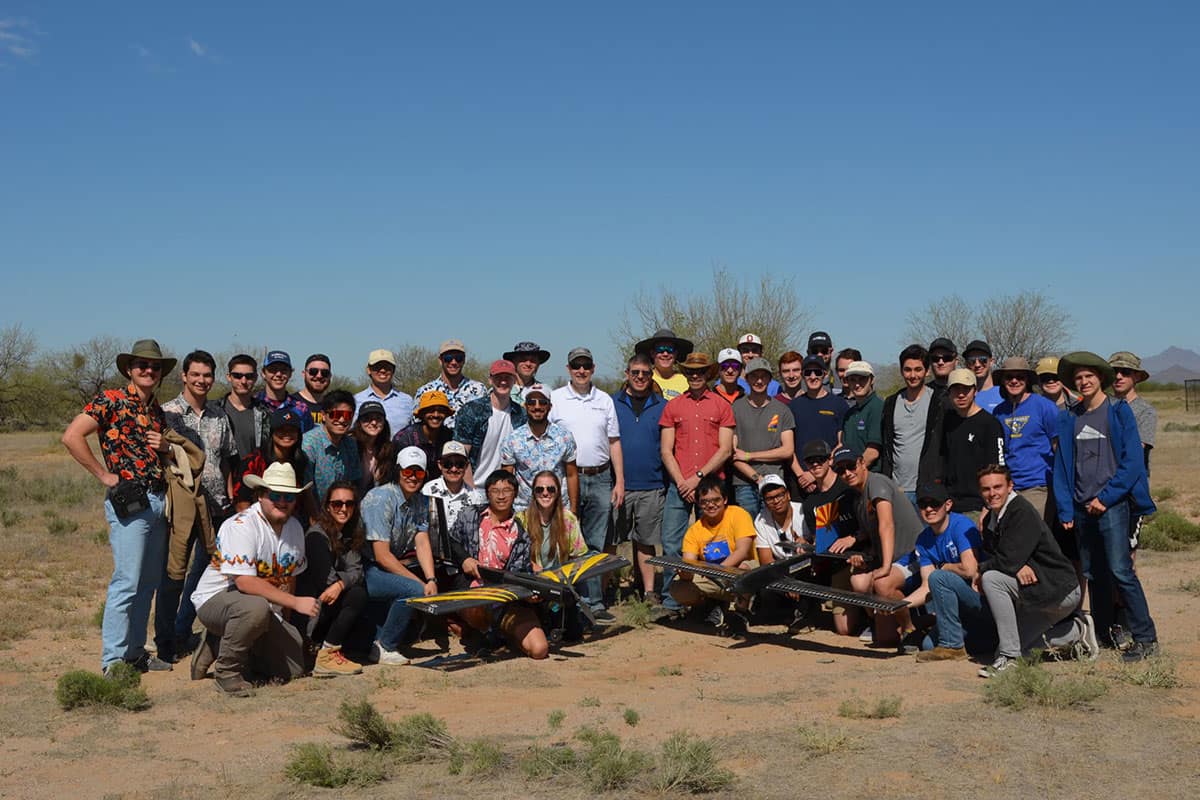 Group of students pose in desert with two aircraft models.