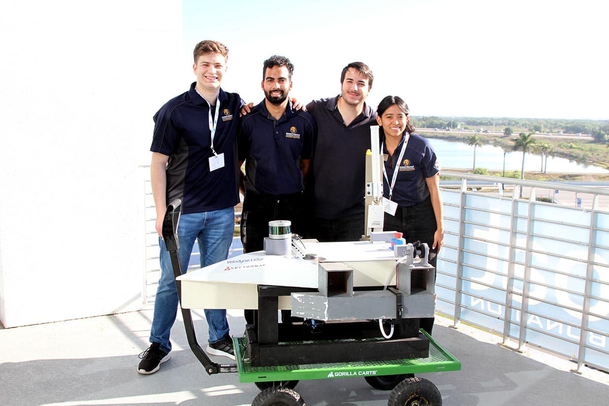 Four students stand behind autonomous boat.