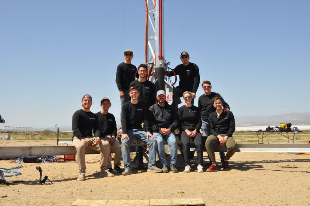 Ten students in black shirts sitting at base of rocket.