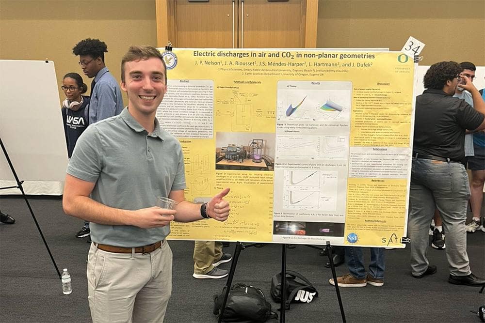 Student stands next to chart displaying electric discharge data.