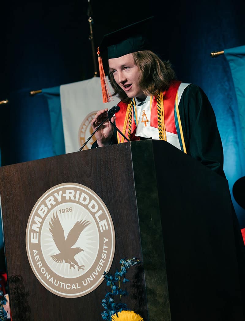 Man in cap and gown speaks at graduation ceremony.