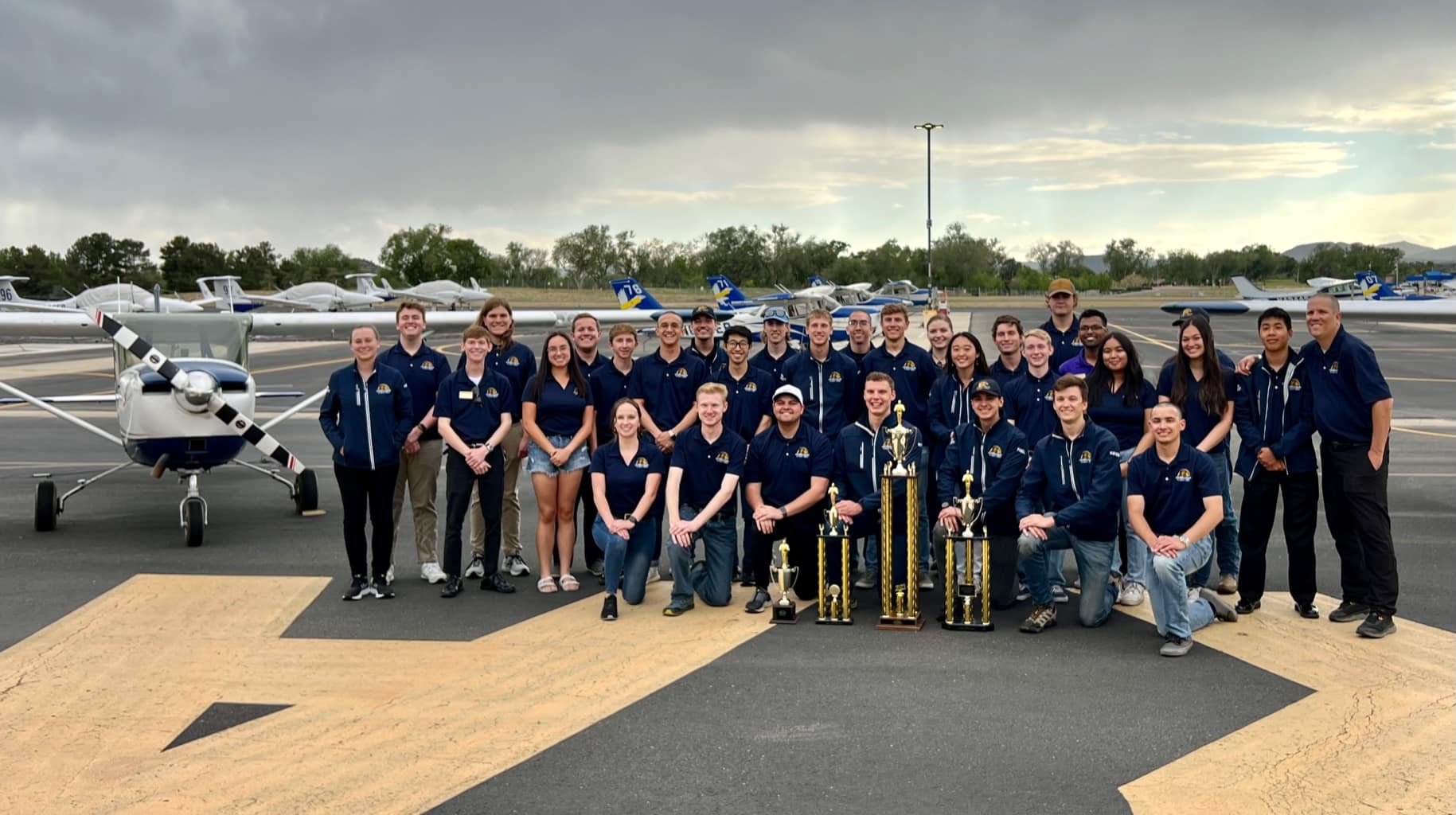 Embry‑Riddle’s Golden Eagles Flight Team poses for picture with trophies on runway.