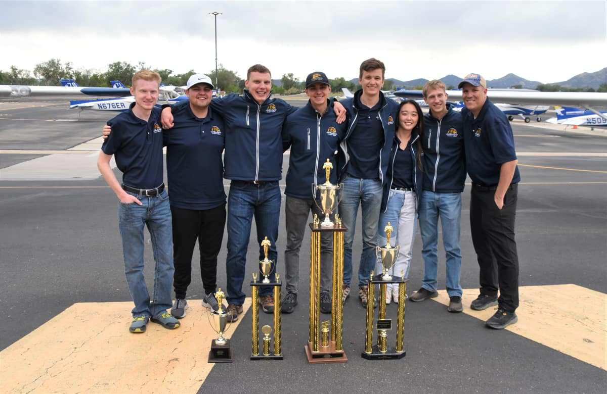 Embry‑Riddle’s Golden Eagles Flight Team seniors pose for picture with trophies on runway.
