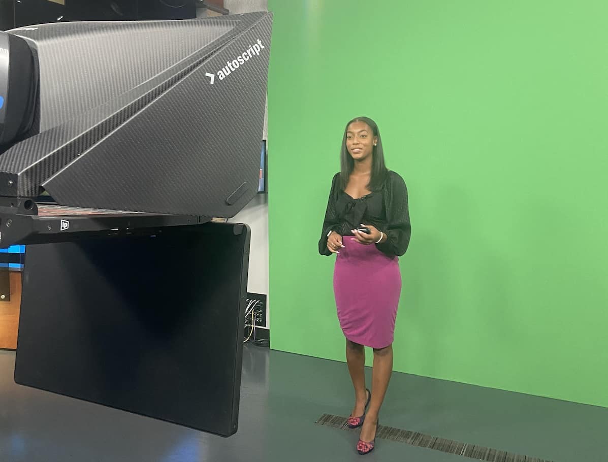 Female student stands in front of green screen.