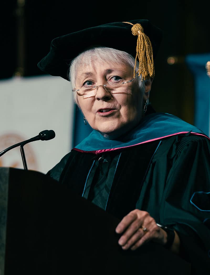 Woman in cap and gown speaks at graduation ceremony.