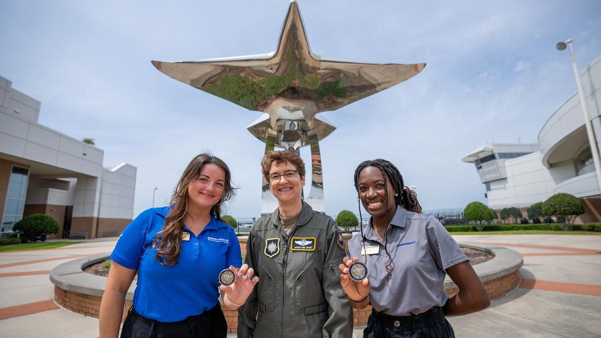 Three women pose in front of statue while holding medals.