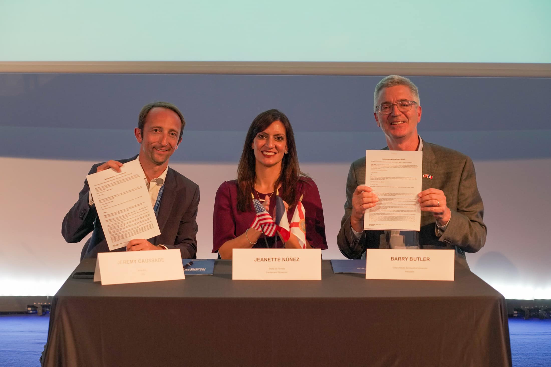 Three people hold up documents after signing a partnership.