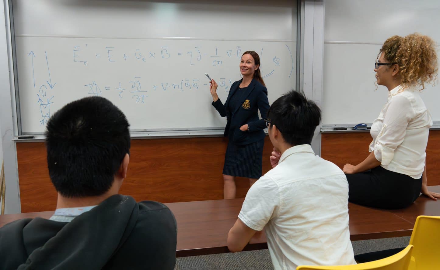Teacher stands at white board teaching students.