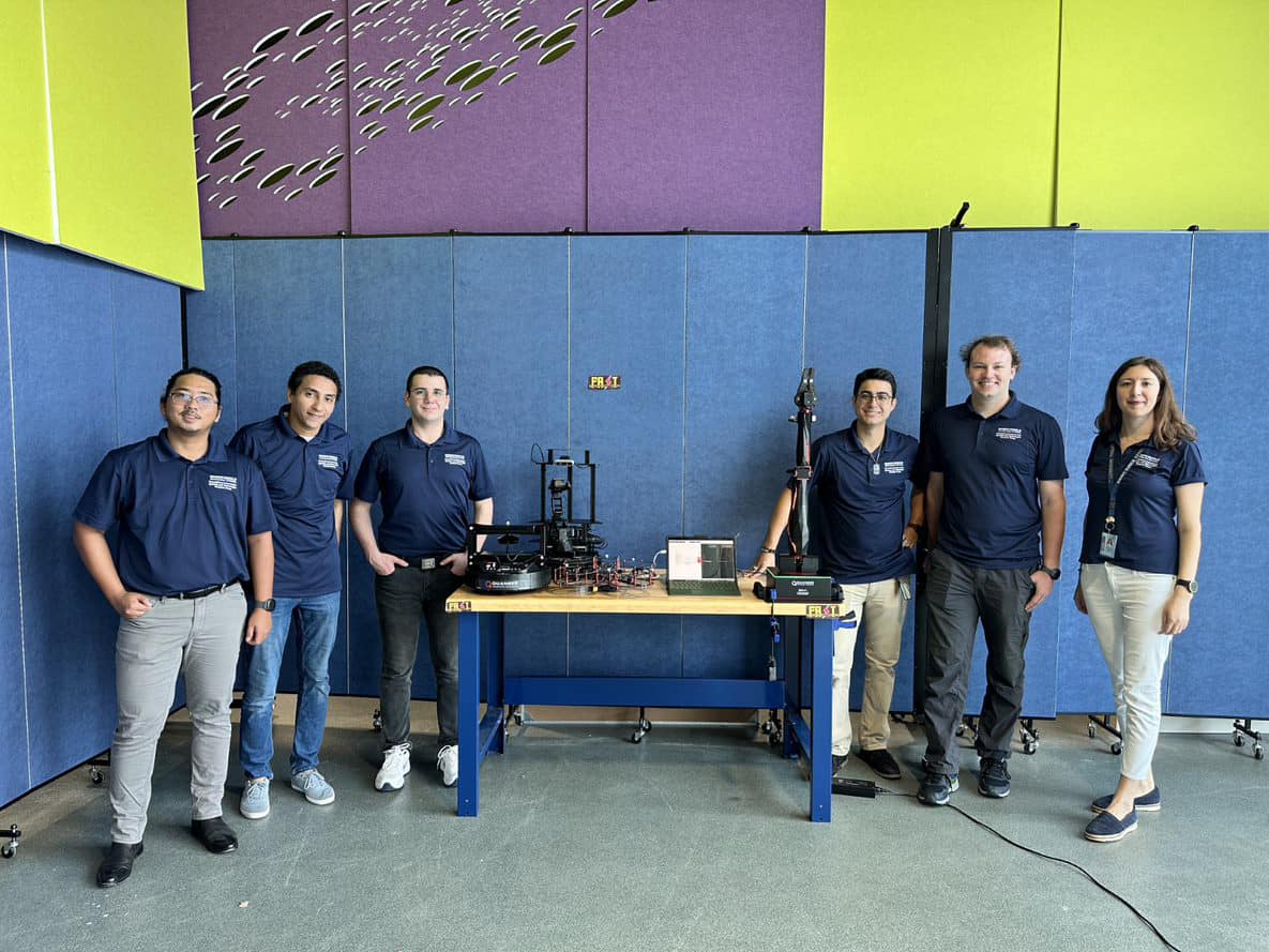 Six students pose around table with robotic equipment.