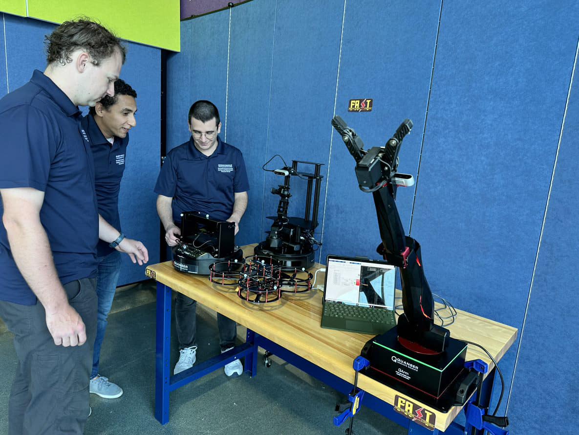 Three students work on robotic arm.