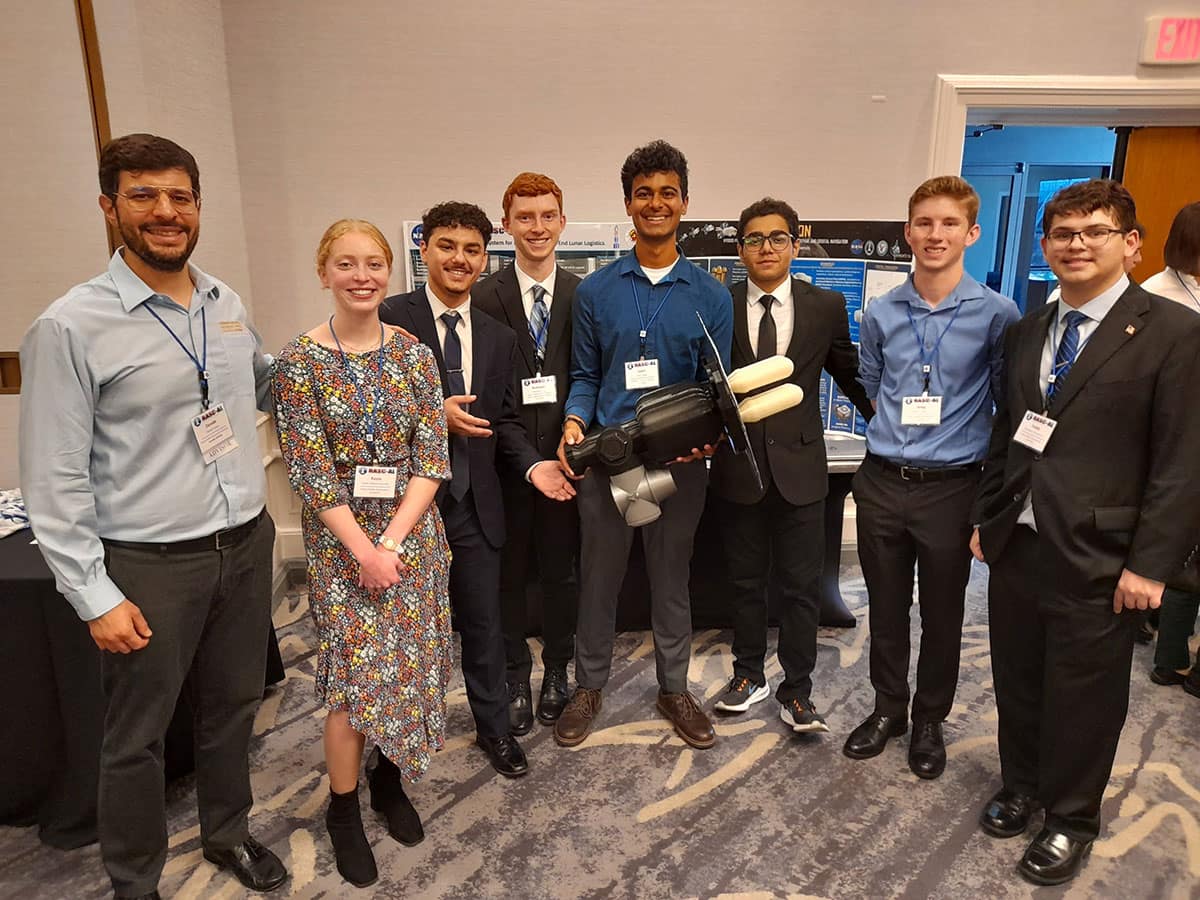 Eight people pose for picture, one holding a model of space technology.